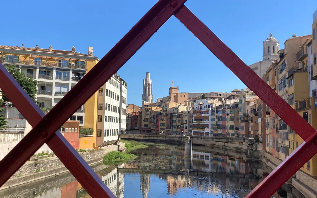 Painted riverside houses and the cathedral tower in Girona, framed by the red iron bridge
