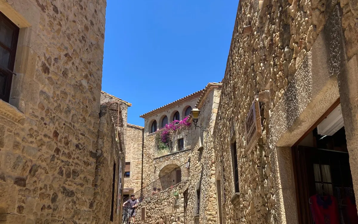 A narrow lane between tall stone walls with flowers on a balcony above
