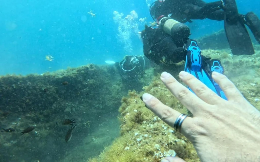 A diver underwater above the rocks, one hand towards the camera