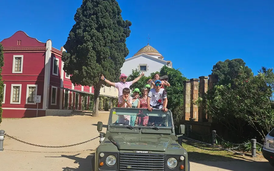 A dark green vintage four-wheel drive parked by a red building