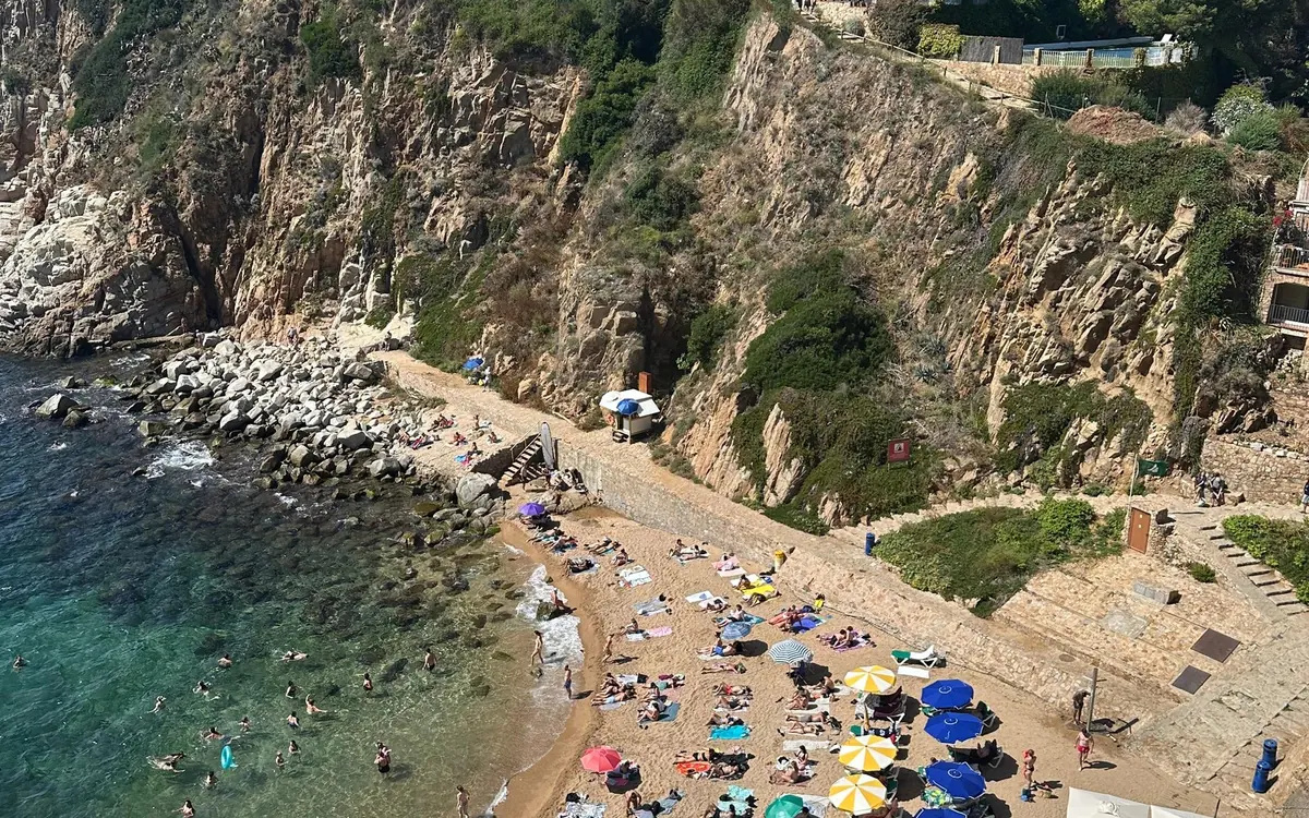 A small sandy cove with parasols and swimmers below steep cliffs
